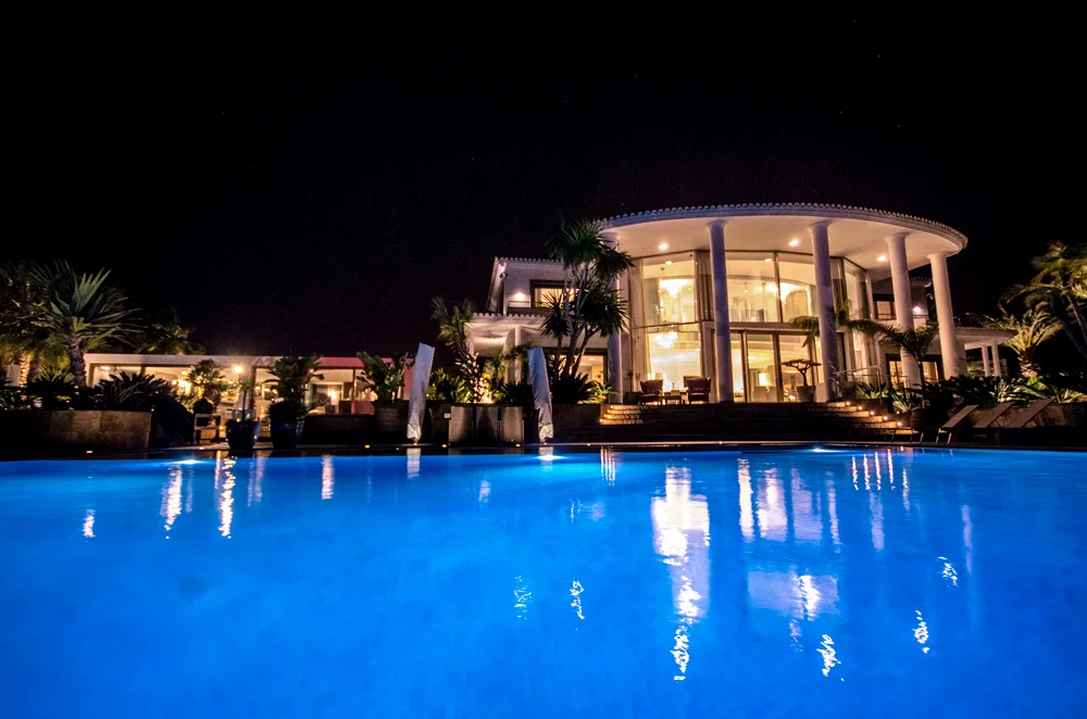 A luxury villa illuminated at night beside a lit swimming pool